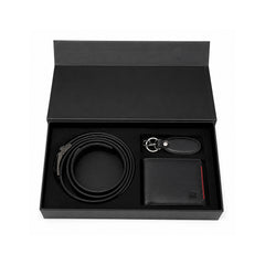 A black leather men's gift set presented in an open black box, including a coiled belt, a bifold wallet, and a keychain with a black leather tag.